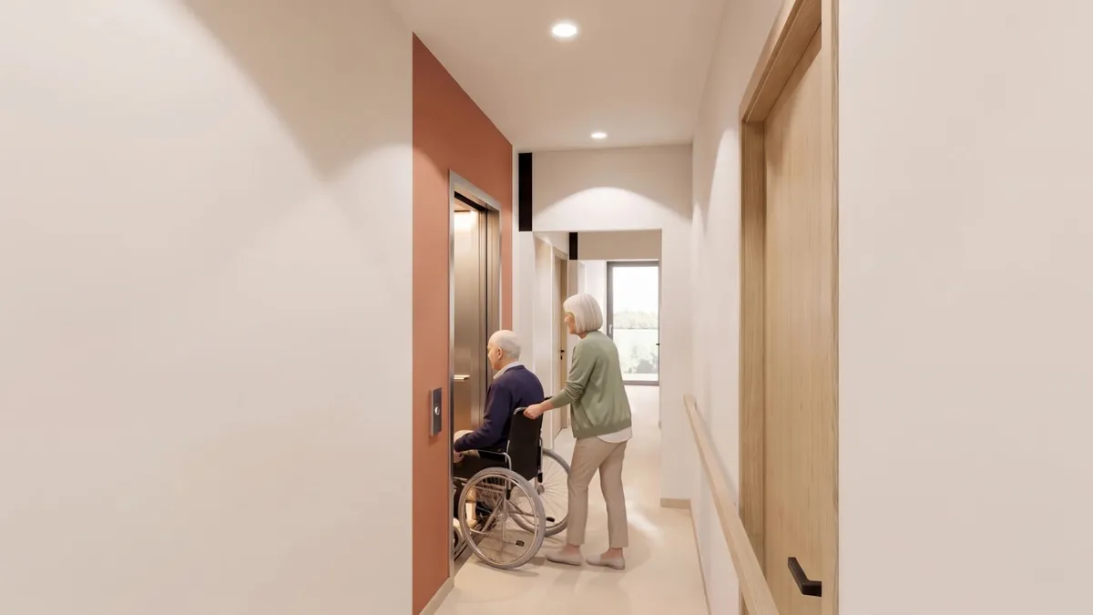 Le couloir de l'étage, au sol de moquette crème : une résidente pousse le fauteuil roulant de son voisin vers l'ascenseur, portes ouvertes.