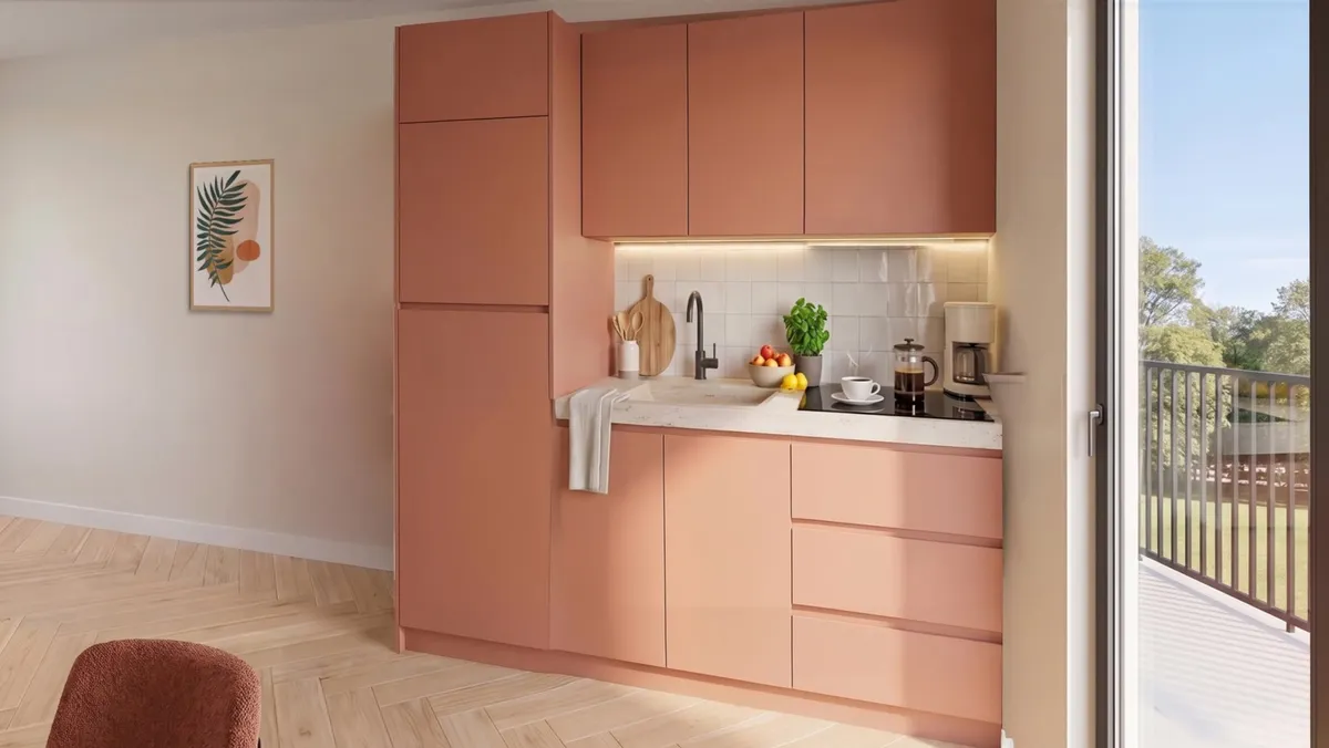 La cuisine du T2 en façades terracotta, près de la baie vitrée du balcon : une cafetière et une tasse sur le plan de travail.