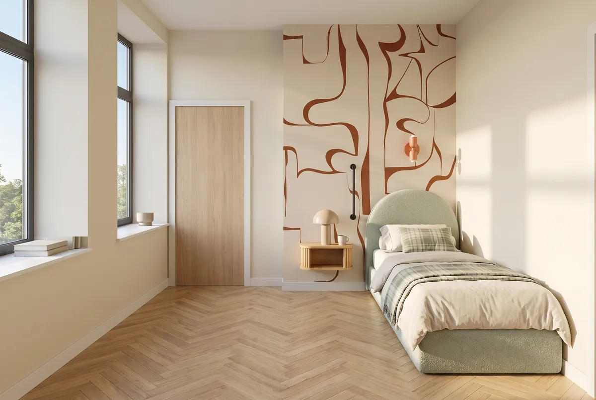 Le coin nuit du T1 : un lit à une place devant un papier peint à motifs terracotta, une barre d'appui et un chevet suspendu à côté, deux grandes fenêtres.